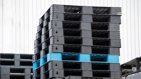 Stack of heavy duty black plastic pallets with one blue rackable pallet outside a warehouse